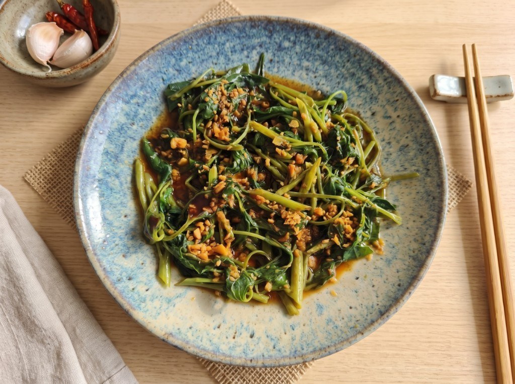 Plate of adobong kangkong: wilted water spinach in glossy soy-vinegar sauce topped with fried garlic