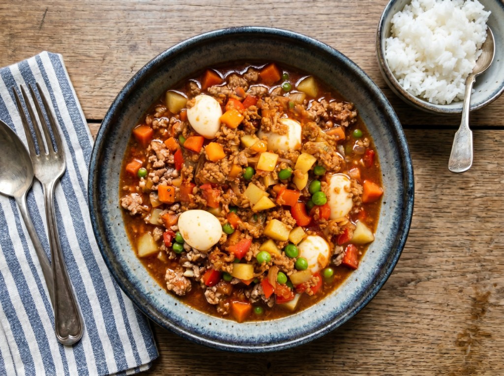 Giniling na baboy in a bowl with ground pork, diced potatoes and carrots, green peas, red bell pepper, and quail eggs in tomato sauce, served with steamed rice