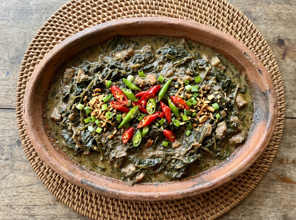 Laing in a clay bowl with creamy coconut sauce, pork, red and green chilies, toasted garlic, and green onions