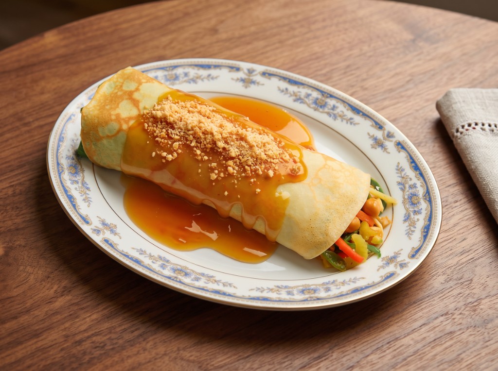 Lumpiang sariwa on a floral plate: one large fresh lumpia roll in a pale crepe wrapper showing carrots, green beans, kamote strips, and garbanzos at the ends, topped with thick glossy sweet sauce and crushed peanuts