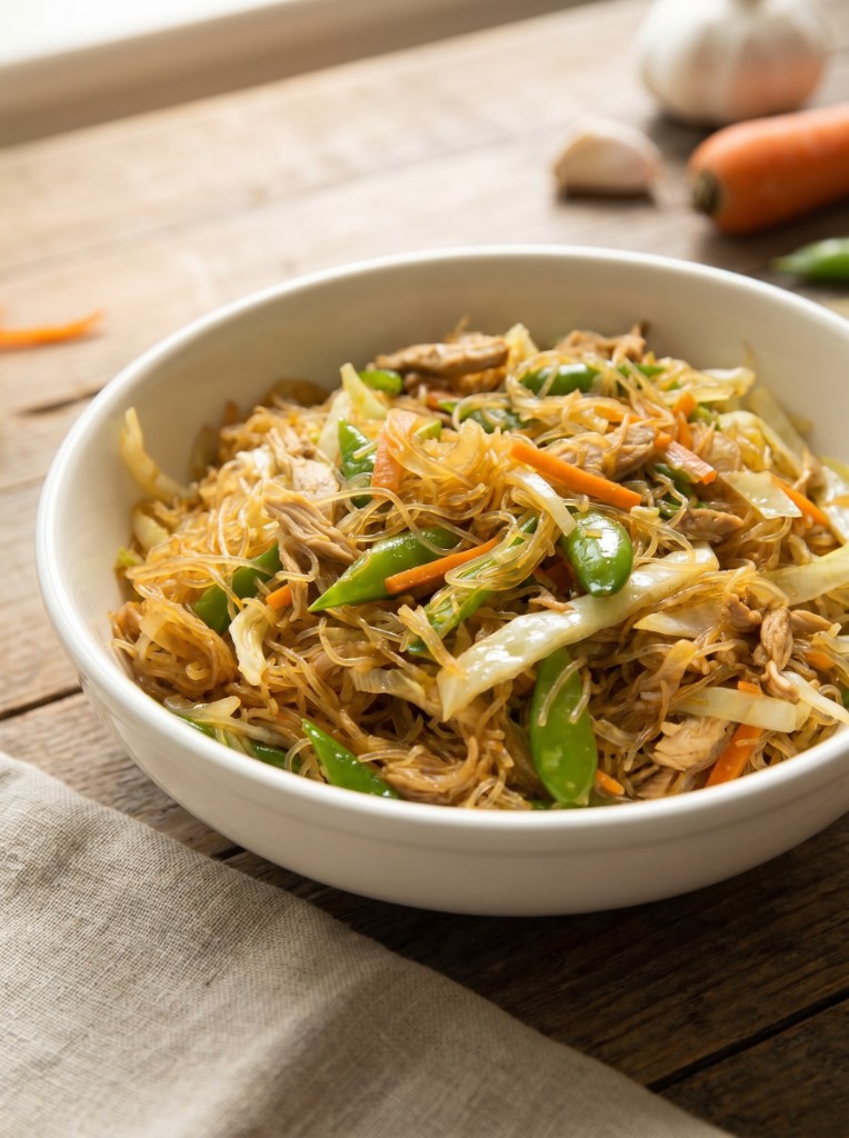 Bowl of Filipino pancit bihon with golden rice noodles, shredded chicken, cabbage, carrots, and snow peas