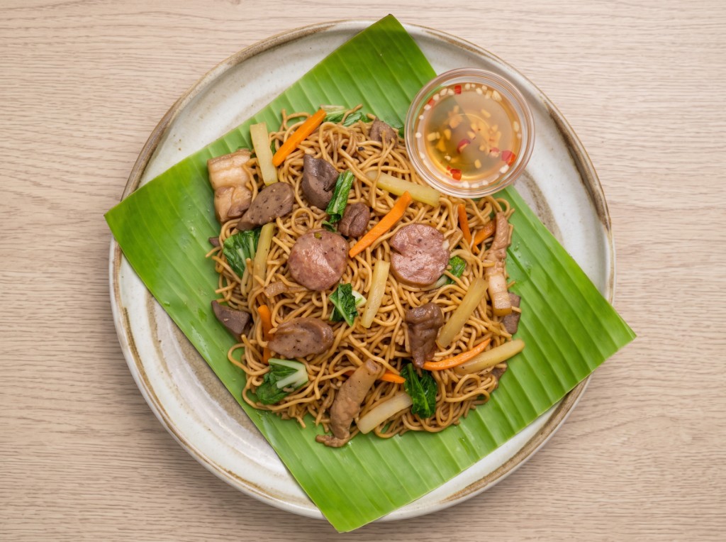 Pancit habhab on a banana leaf: toasted miki noodles with pork belly, liver, sausage, carrots, sayote and pechay, vinegar dip with garlic and chili in a glass ramekin