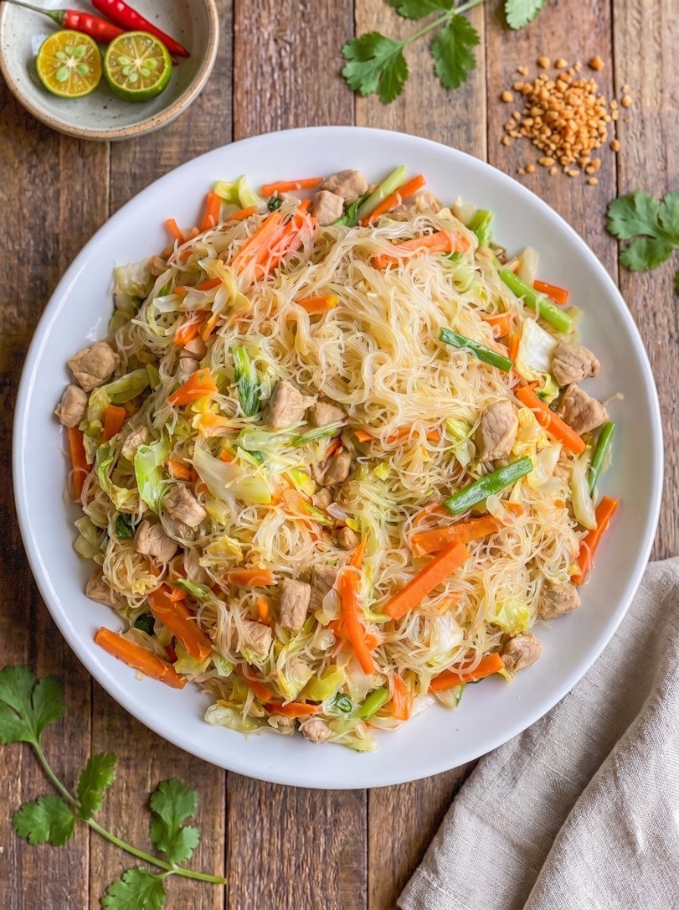 Bowl of pancit sotanghon: translucent glass noodles with carrot, cabbage, and chicken, calamansi and toasted garlic on the side