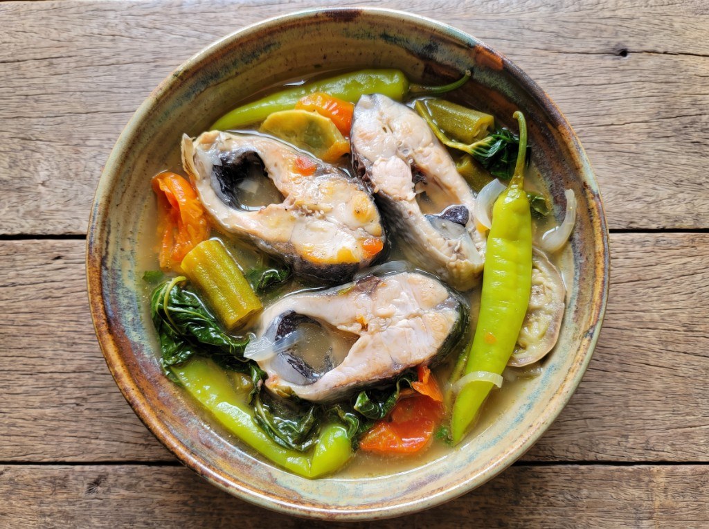 Bowl of sinigang na bangus with milkfish, radish, sitaw, okra, tomatoes, and kangkong in sour broth