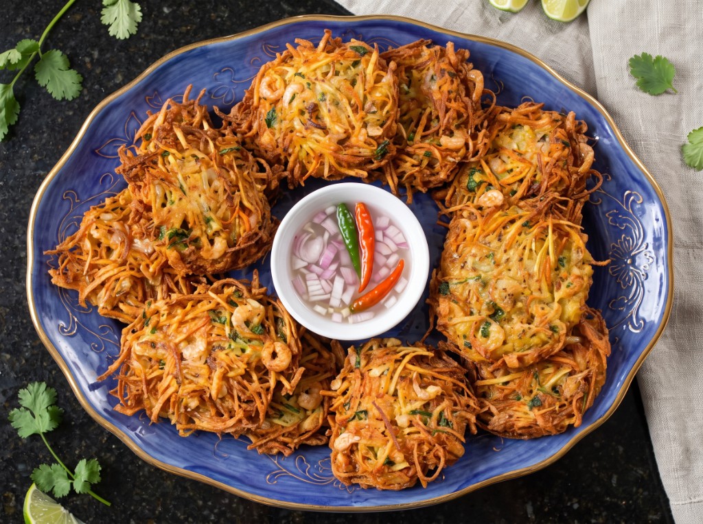 Crispy ukoy shrimp fritters in a ring on a blue gold-rimmed platter, center bowl of vinegar with minced onion and red and green chilies, cilantro and calamansi on the side